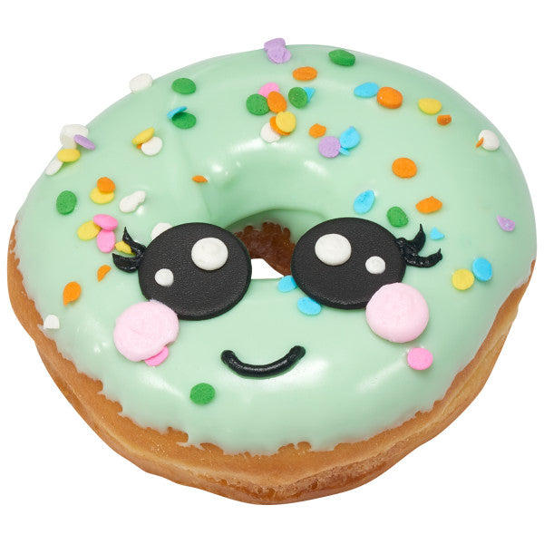 A donut with a smiley face decorated in green frosting and pastel sequin sprinkles