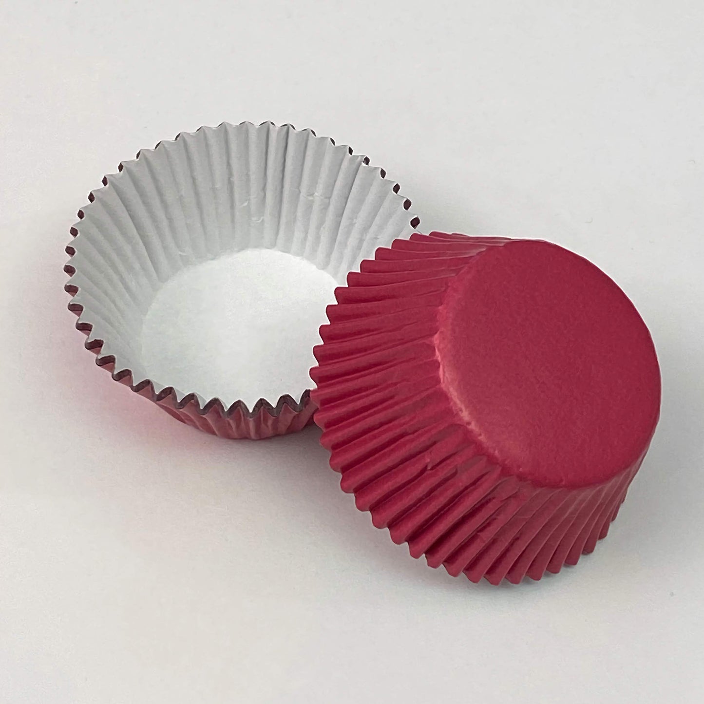 Standard-sized pink foil baking cups, shown both open and stacked. The interior is white, while the exterior has a shiny, reflective pink surface, perfect for adding a touch of elegance to baked goods.