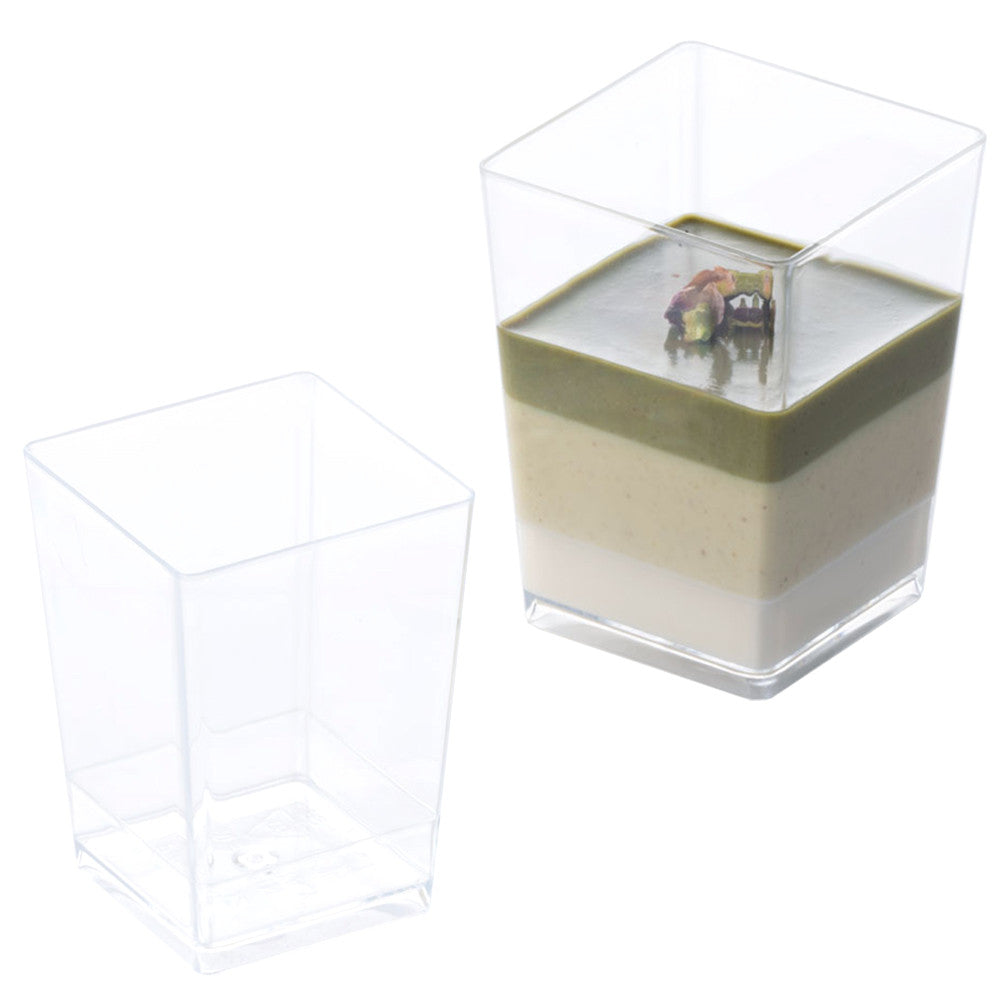 Two clear square plastic dessert cups, one empty and one filled with layered green and cream dessert topped with chopped nuts, on a white background.