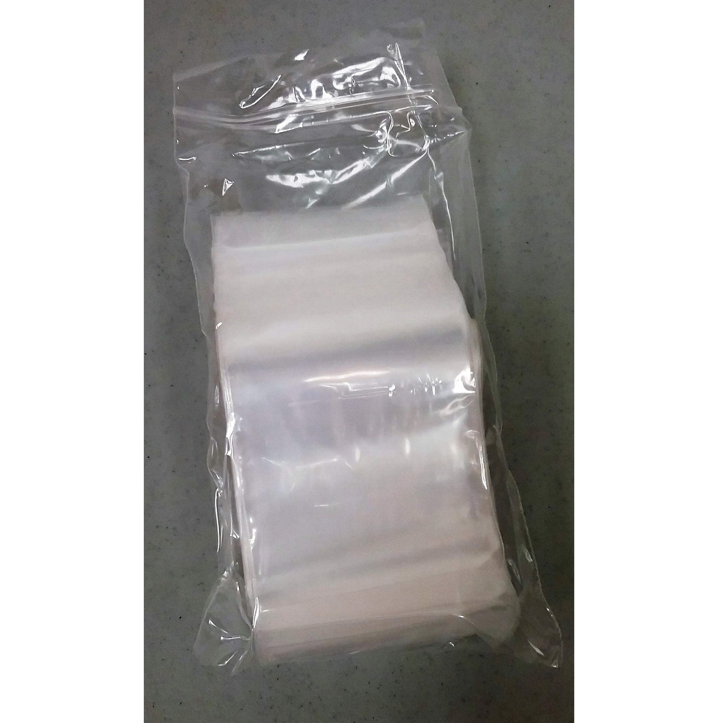 An image of a sealed package containing 50 clear poly zip-top bags. The bags are neatly stacked and enclosed in a plastic wrap, with a slight transparency that shows the zip-top closures. They are presented on a grey, speckled surface, indicative of a sturdy, utilitarian design for storage or organizational purposes.