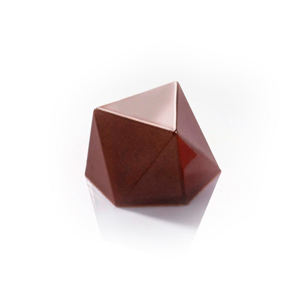 Finished geometric chocolate bonbon with multiple flat facets and a glossy dark chocolate finish, shown on a white reflective surface.