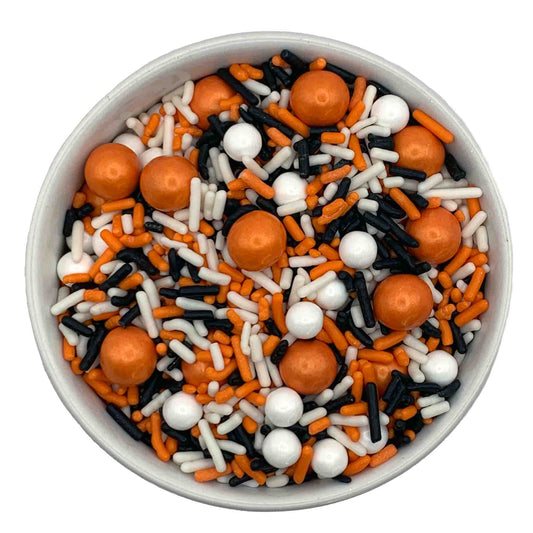 A bowl of sprinkles featuring white sugar pearls, orange sixlets, and a mix of white, black, and orange jimmies, perfect for decorating fall-themed treats and desserts.