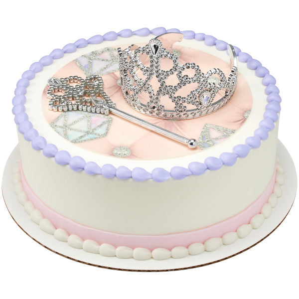 Round princess-themed cake topped with a tiara and wand on a pink background