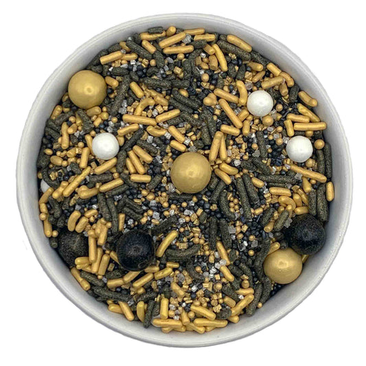 A bowl of sprinkles featuring gold sixlets, white sugar pearls, black and gold jimmies, gold nonpareils, and a mix of gold and silver sanding sugar, perfect for adding a luxurious touch to desserts.