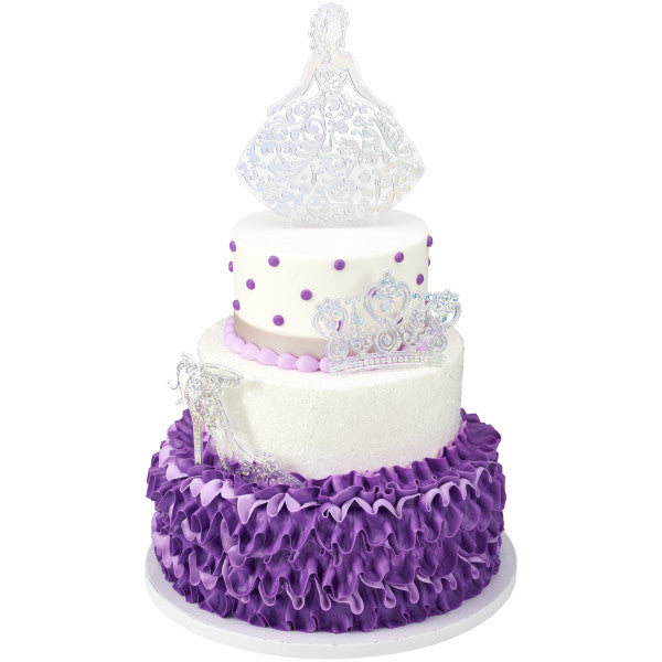 Three-tiered white and purple Quinceañera cake decorated with silver toppers including girl, crown, and shoe.