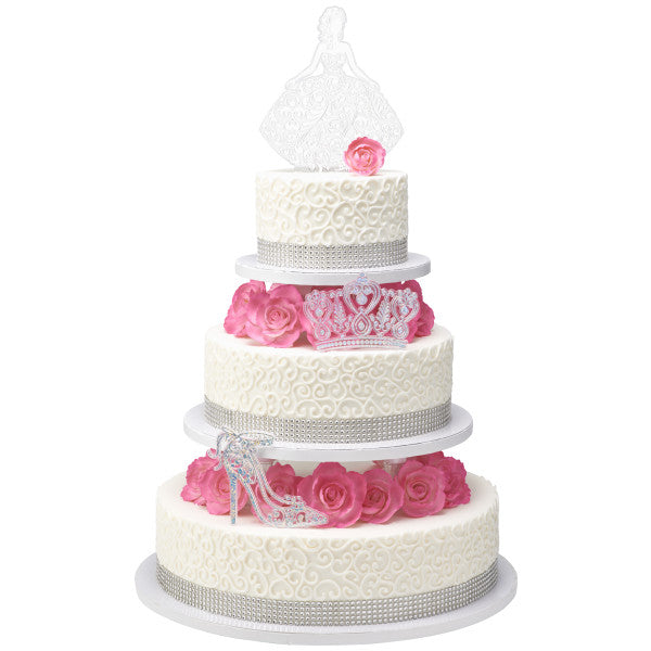 Tall four-tier white cake with pink roses and silver Quinceañera toppers: girl, tiara, and high heel shoe.