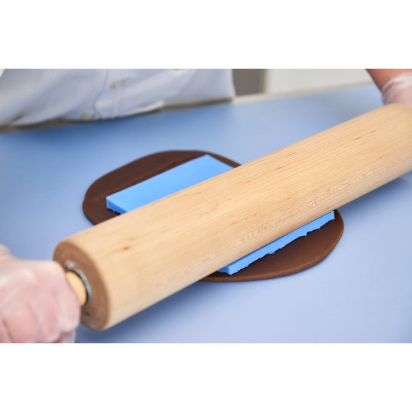 Rolling pin pressing bark texture mat into dark brown fondant