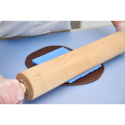 Rolling pin pressing bark texture mat into dark brown fondant