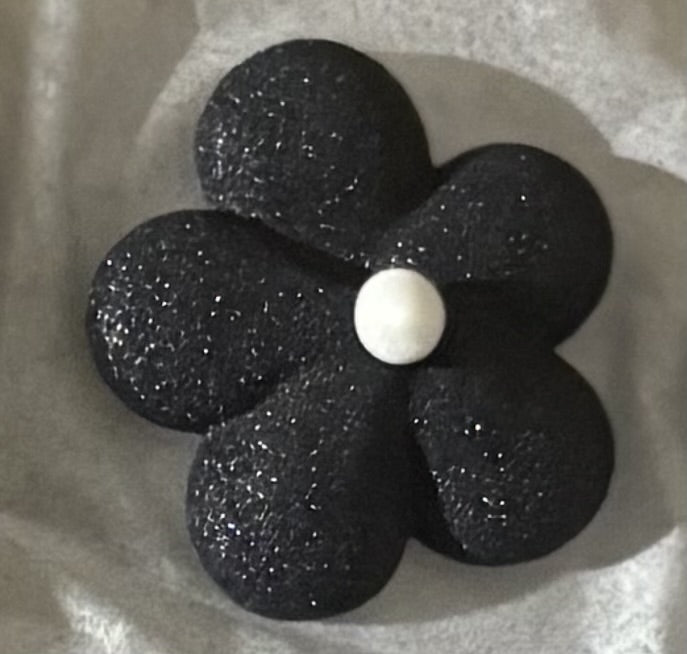 Close-up of a delicate royal icing flower in black with a white center.