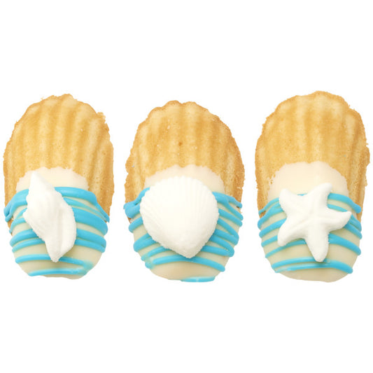 Three madeleine cookies dipped in white chocolate and blue drizzle, each topped with a different white sugar sea-themed decoration.