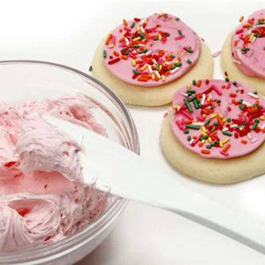 White spatula spreading pink frosting on sugar cookies with sprinkles.
