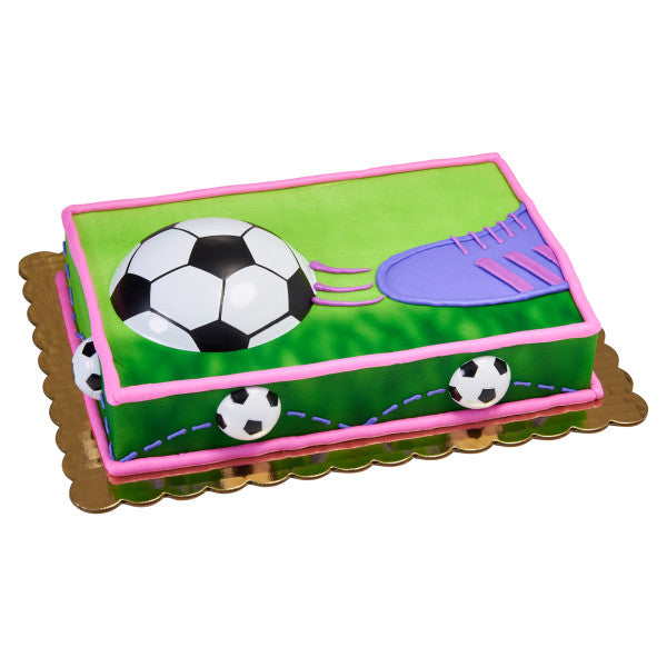 Vibrant soccer ball cake, featuring a black and white soccer ball half-embedded in green icing with grass details and a pink border. Ideal for soccer fans and sports-themed parties.