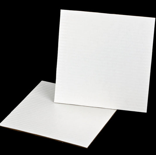 White square corrugated cake pads made from coated cardboard, shown on a black background for bakery and catering use.