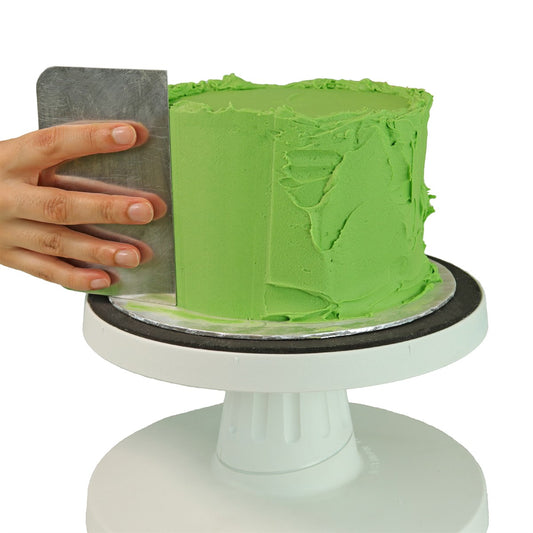 Hand using PME side scraper to smooth green buttercream on a cake for a clean, professional finish.