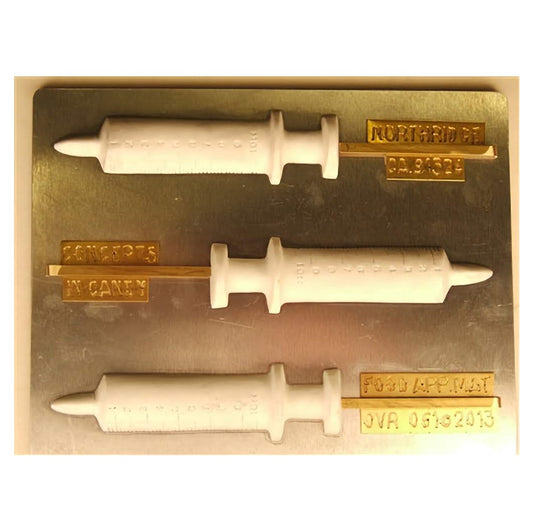 Image displays a chocolate mold designed to create syringe-shaped suckers. The mold includes four syringe cavities, each detailed with markings along the barrel, a plunger, and a needle tip. The finished suckers would resemble medical syringes, making them an interesting choice for themed parties or educational events related to health and medicine.