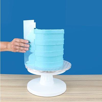 PME Extra Wide Stripes Side Scraper being used to create broad horizontal stripes on a tall blue buttercream cake.