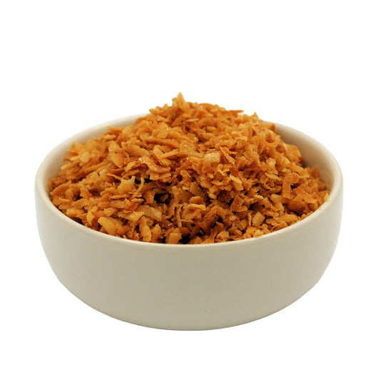 Side view of a white bowl filled with finely shredded toasted coconut flakes, golden brown in color.