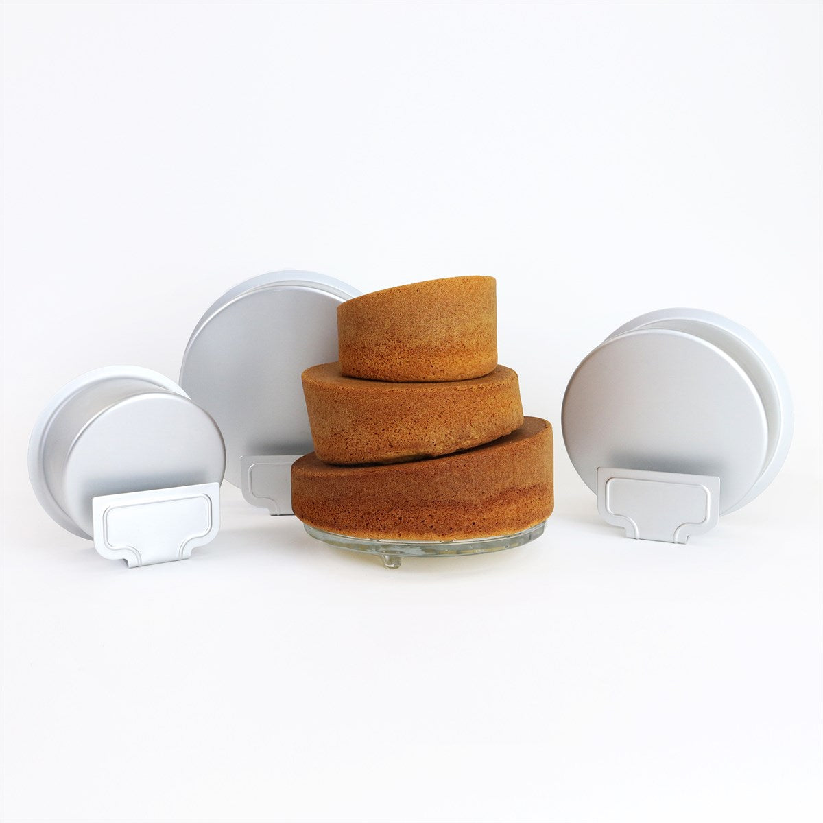 Baked topsy turvy cakes in three sizes displayed next to their angled pans, showcasing the sloped effect and professional finish.