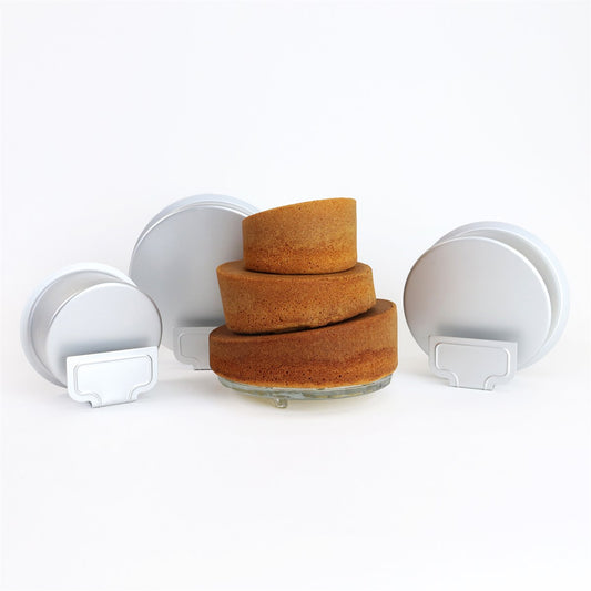 Baked topsy turvy cakes in three sizes displayed next to their angled pans, showcasing the sloped effect and professional finish.