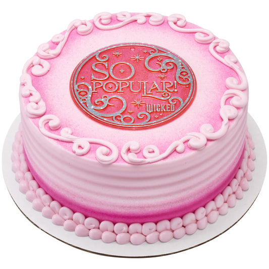 Pink ombré round cake with piped swirls and bead border, topped with the bright pink circular “SO POPULAR” Wicked plaque.