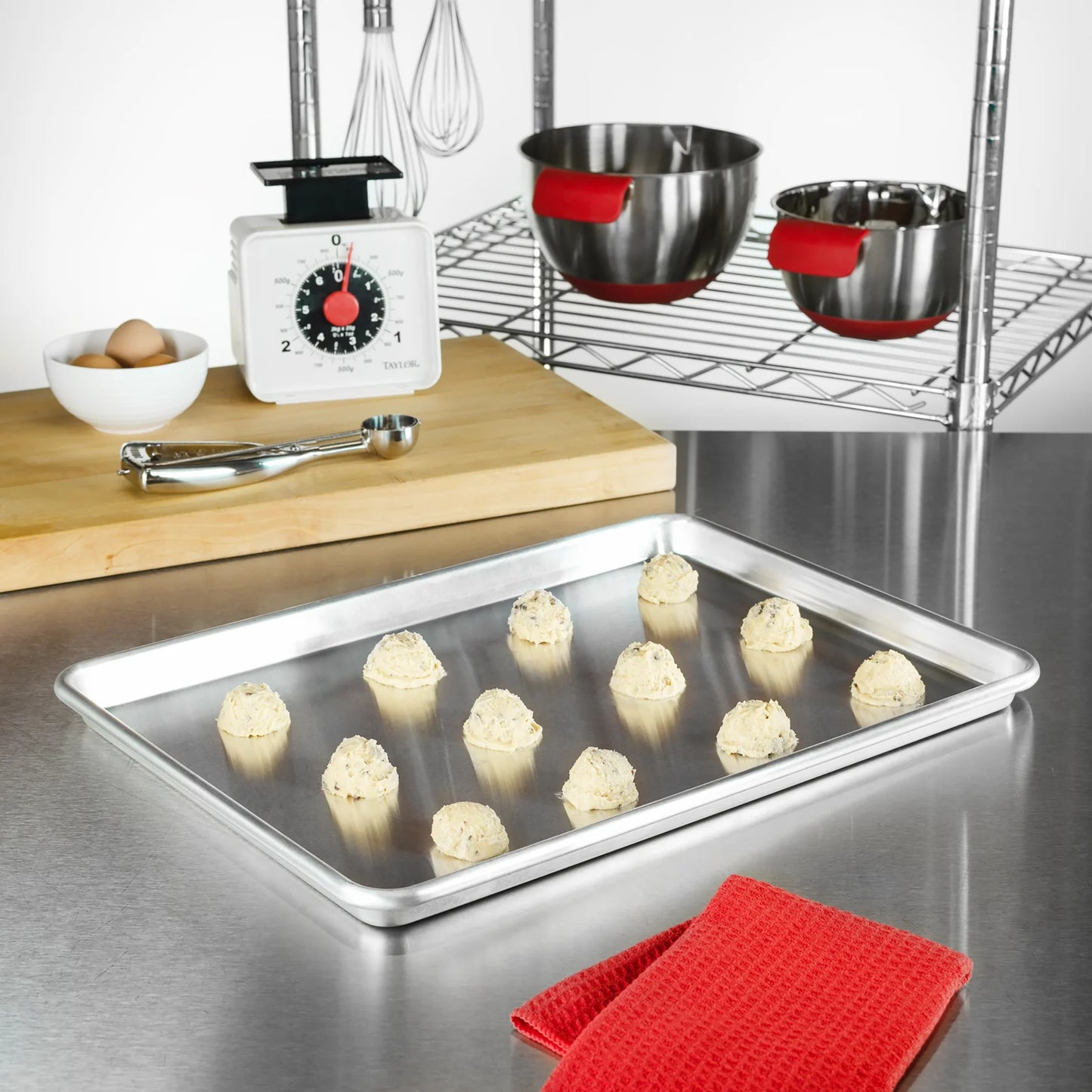 Quarter sheet pan on a kitchen counter with scoops of cookie dough, surrounded by baking tools and ingredients