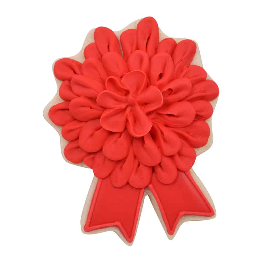 Decorated cookie in the shape of a ribbon award, with a red icing flower-like rosette and detailed ribbon tails.
