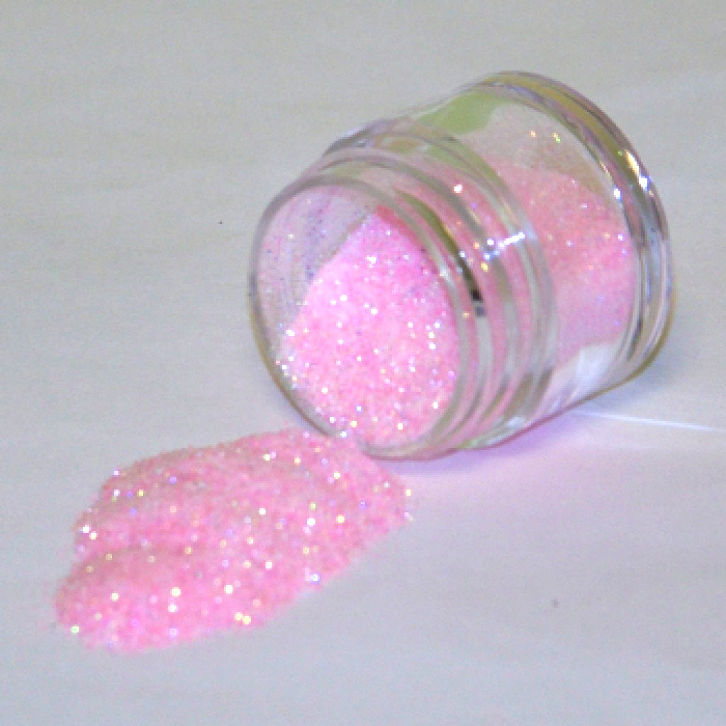 Clear jar tipped on its side with baby pink galaxy glitter dust spilled onto a white surface.