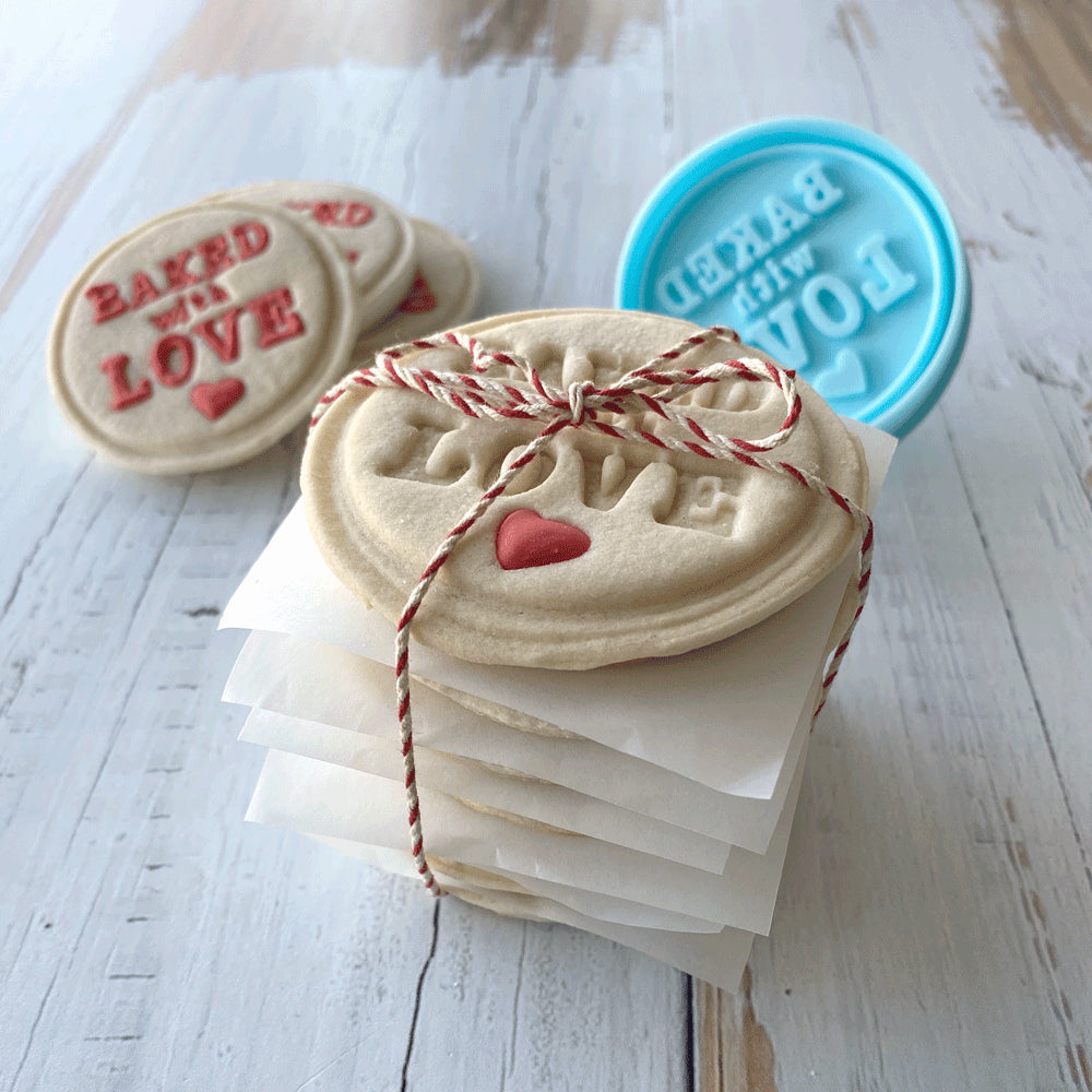 Stack of embossed sugar cookies with red heart details, wrapped in twine, with the "Baked with Love" stamper in the background.