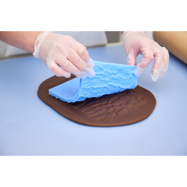 Hands lifting bark impression mat to reveal woodgrain texture in fondant