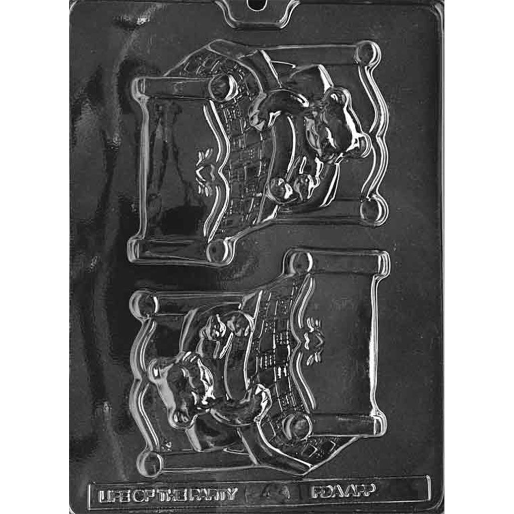 Clear plastic chocolate mold with two large cavities shaped like a teddy bear tucked in bed under a quilted blanket, shown on a dark background.