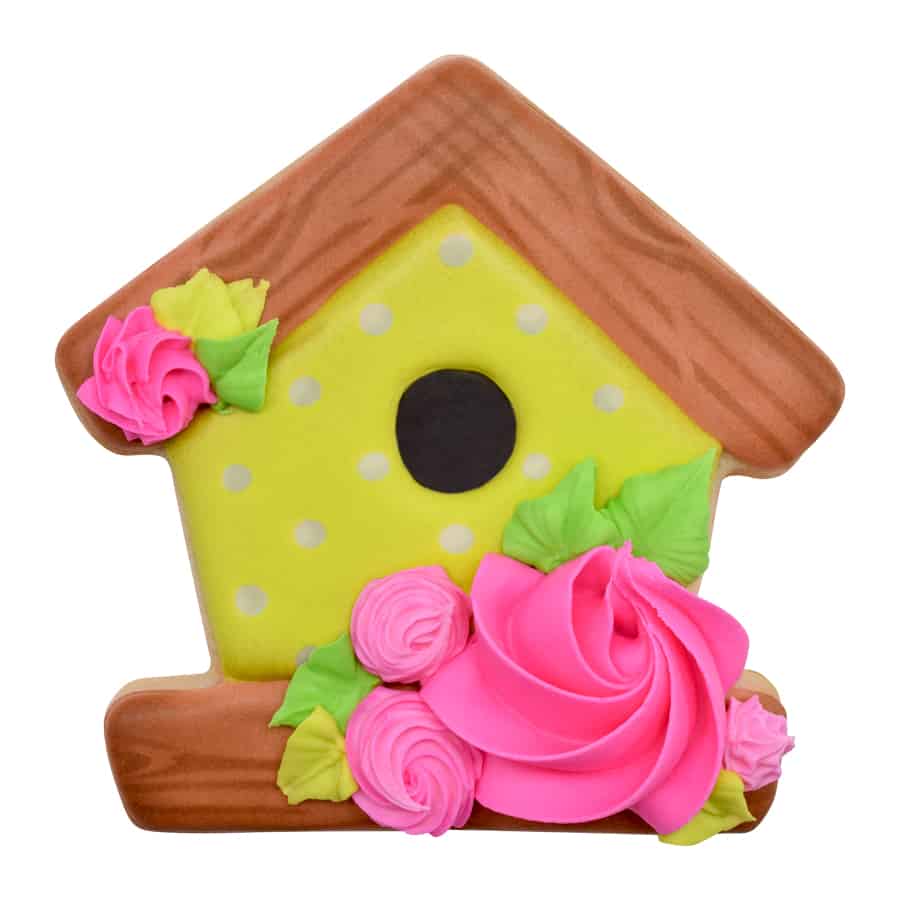 Decorated birdhouse-shaped cookie with yellow icing, a brown roof, and pink floral details.