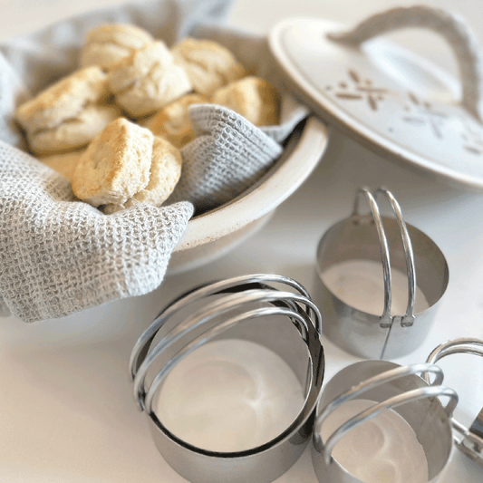 Biscuit cutter set displayed next to freshly baked biscuits in a cloth-lined bowl.