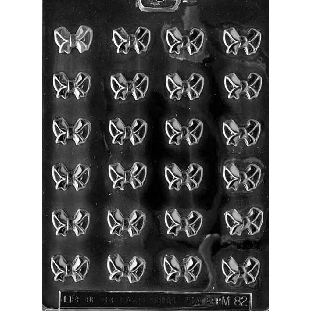 Clear plastic chocolate mold with 24 small bow-shaped cavities arranged in rows, designed for making bite-sized bow chocolates for decorating desserts.