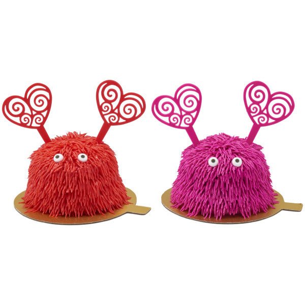 Two fuzzy monster treats with heart antennae sitting on gold boards
