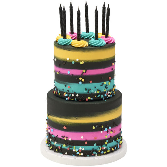 Two-tiered birthday cake with colorful icing and sprinkles, topped with black spiral Over the Hill candles.