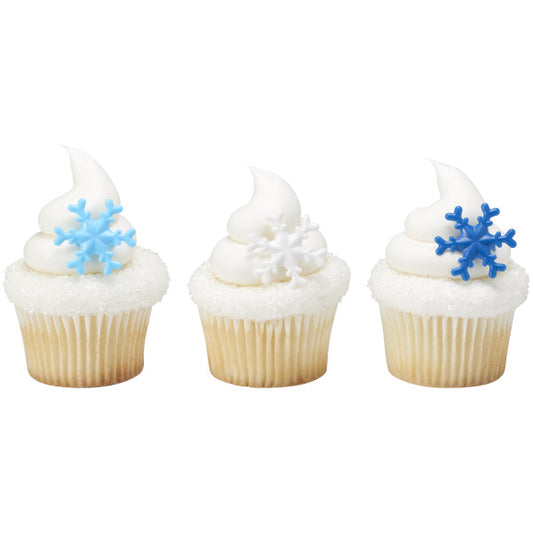 Three vanilla cupcakes topped with white frosting and sugar sprinkles, each decorated with a snowflake ring in light blue, white, or dark blue.