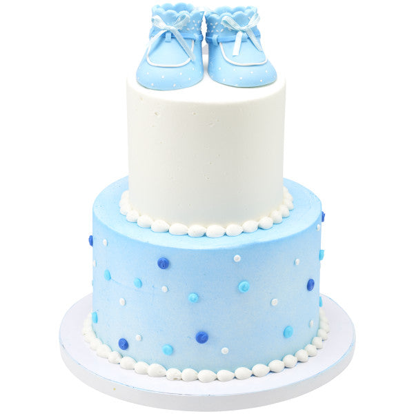 Two-tiered cake with white and blue frosting, topped with the blue baby booties cake decoration