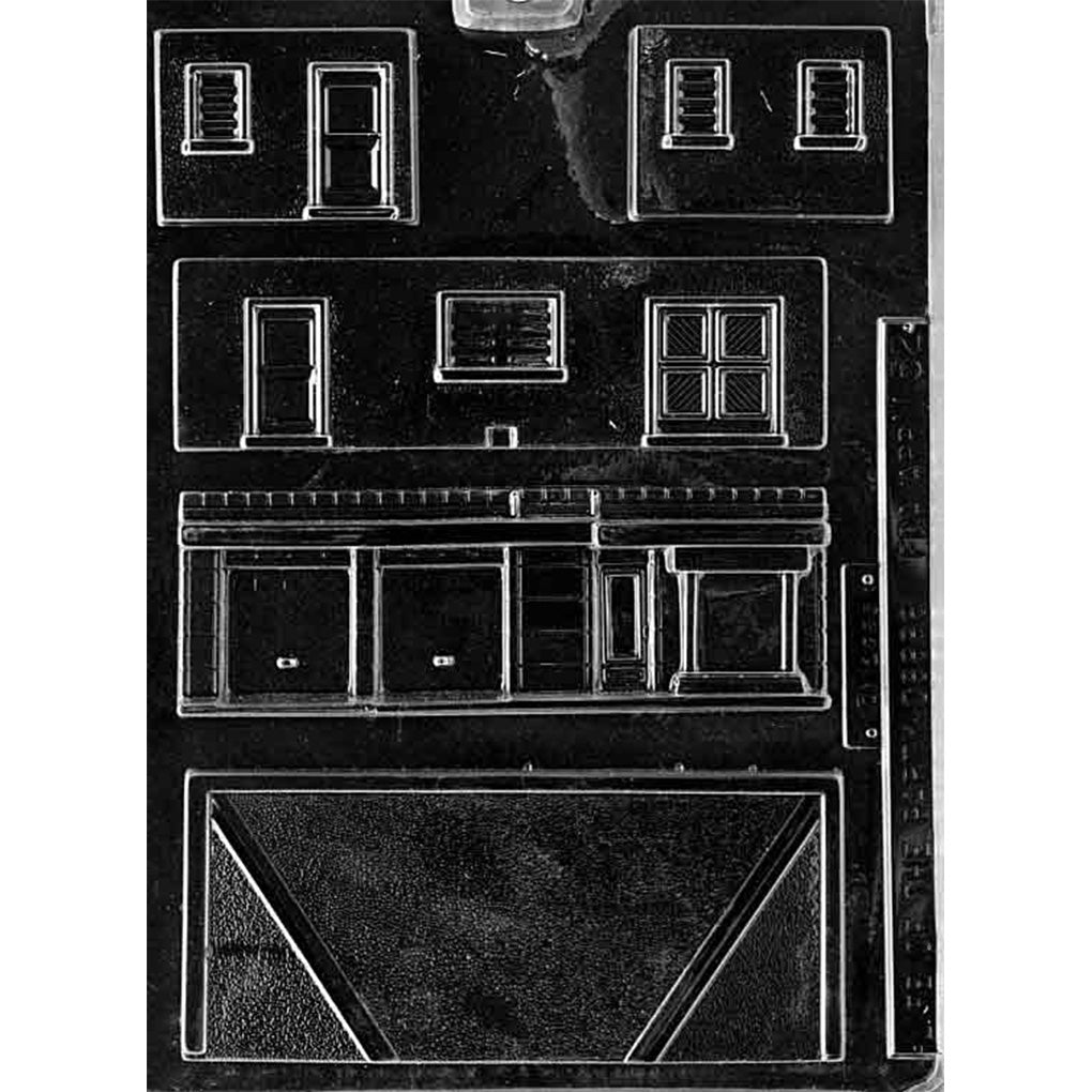 Clear plastic chocolate mold with garage and shop building panel cavities, including a wide front panel with multiple garage doors, smaller wall pieces with windows and doors, and a large roof panel for assembling a 3D building.
