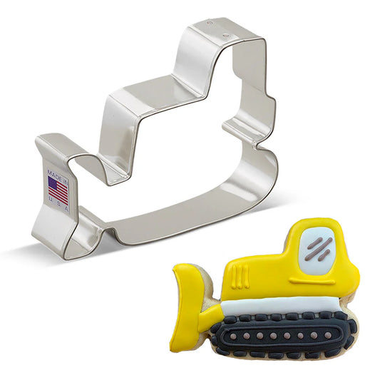 Metal bulldozer cookie cutter next to a decorated sugar cookie shaped like a bulldozer, featuring yellow, black, and white icing details.