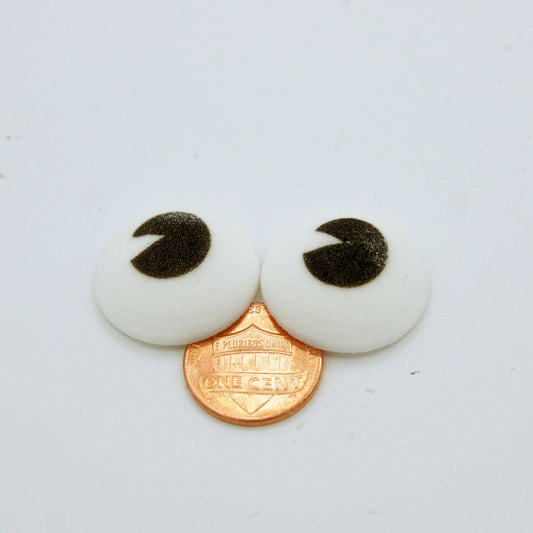 Two 1" edible candy eyes placed on a penny, showing their large size and crescent-shaped black pupils for whimsical dessert decoration.