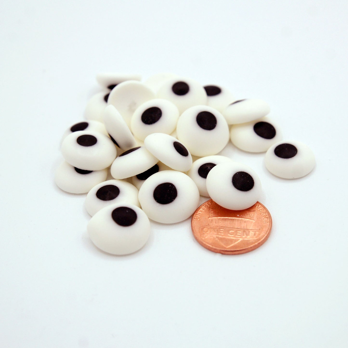 A close-up of 1/2" edible candy eyes next to a penny for size reference, showing large royal icing eyes perfect for decorating baked treats.