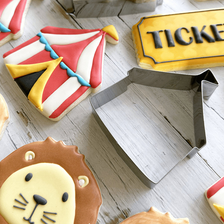 Decorated circus tent-shaped cookies with bright red, white, and blue icing, surrounded by other carnival-themed treats.