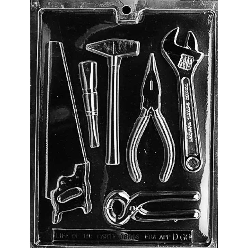 Clear plastic chocolate mold photographed against a black background, featuring assorted hand-tool cavities including a hand saw, screwdriver, hammer, needle nose pliers, combination pliers, and a crescent wrench.