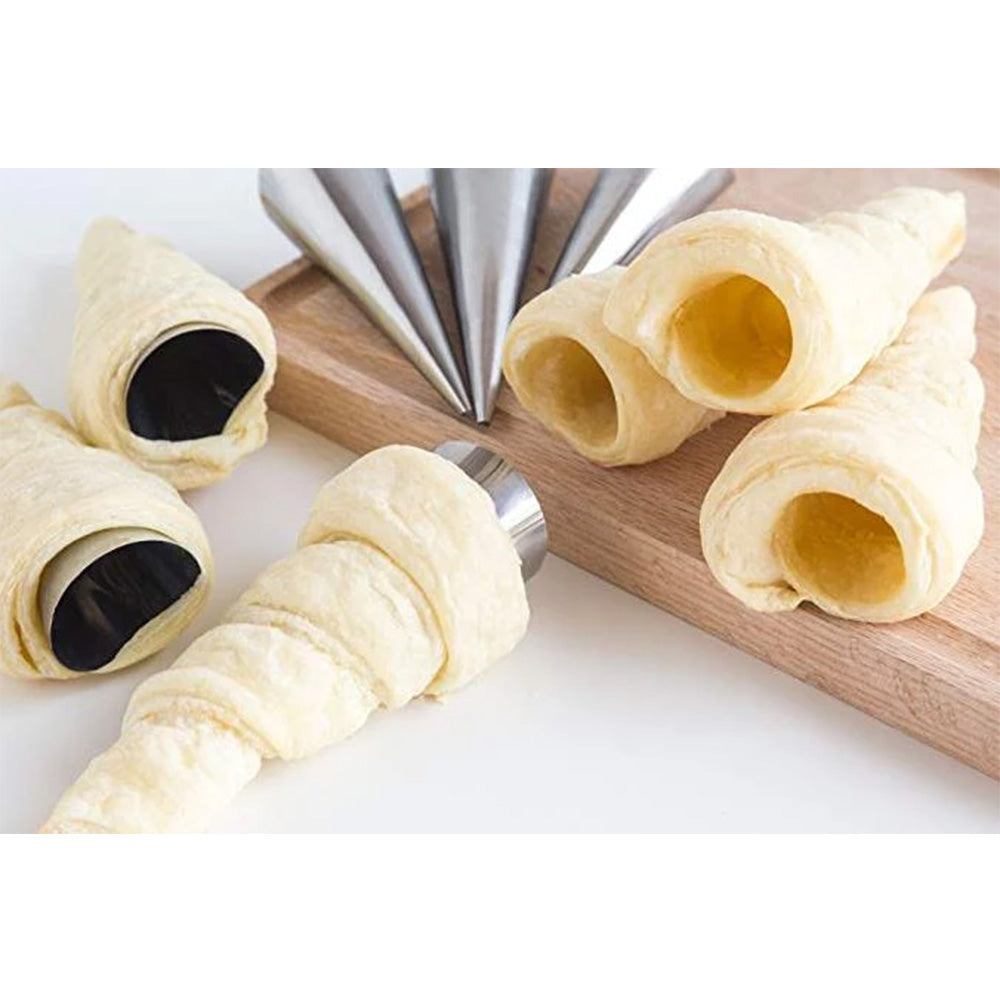 Baked cream horns wrapped around metal molds, shown next to additional unfilled pastry cones on a wooden cutting board.
