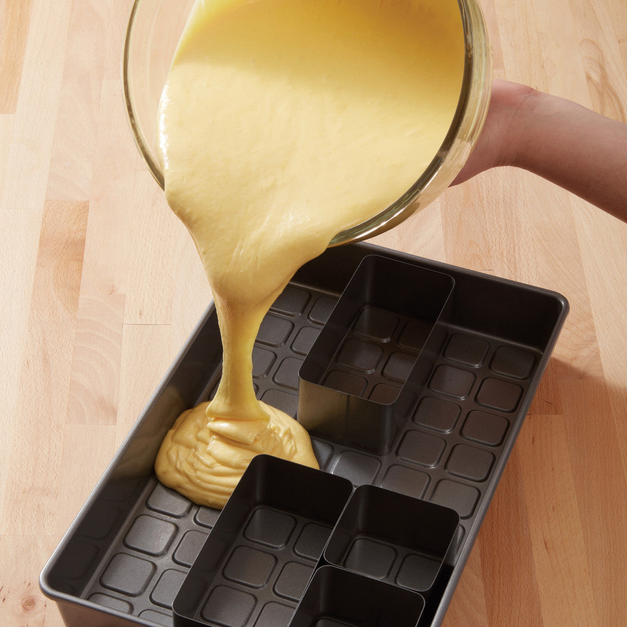 Yellow cake batter being poured into configured inserts inside the rectangular cake pan.