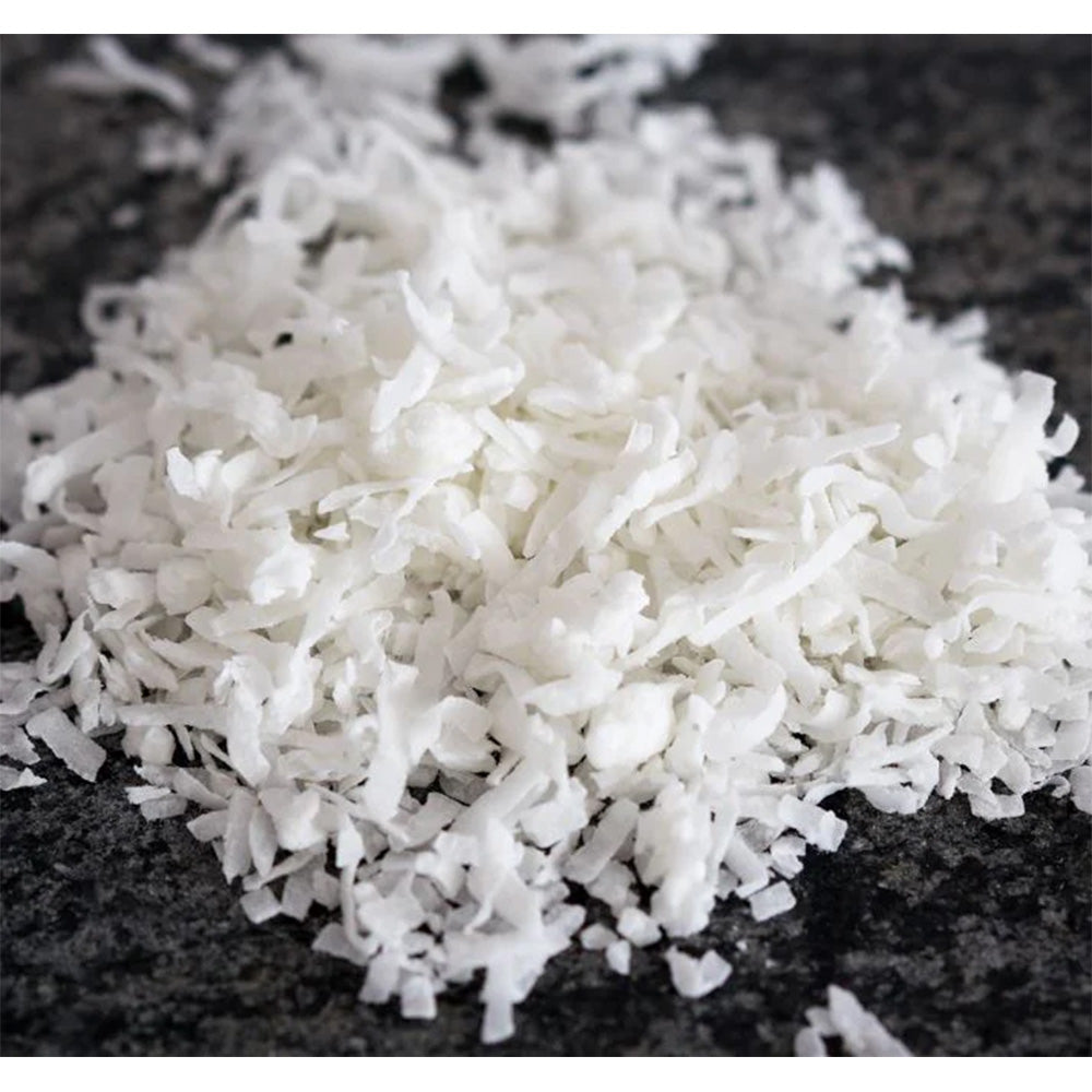 Close-up of desiccated coconut flakes on a dark surface, unsweetened and finely shredded for baking and cooking