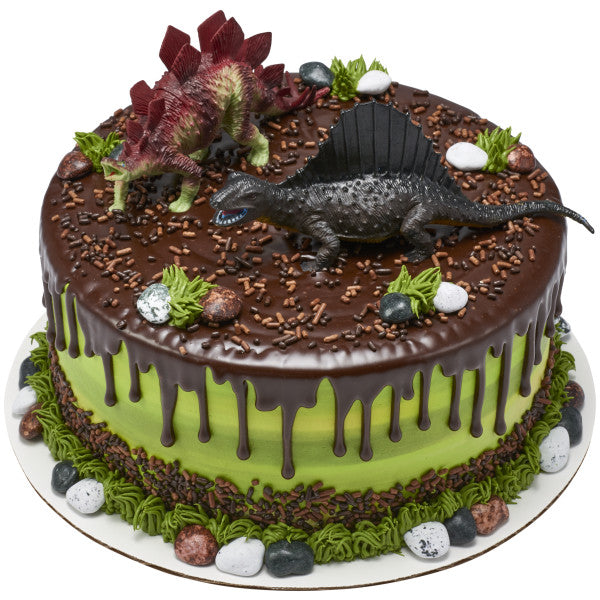 Chocolate-drizzled green cake topped with dinosaur figures, candy rocks, and piped greenery.