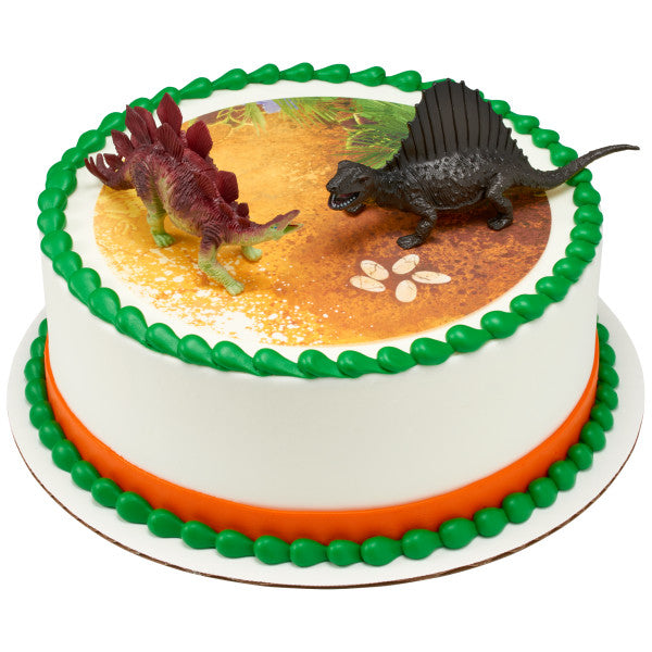 Round cake with green and orange trim, topped with two dinosaur figures on a printed prehistoric scene.