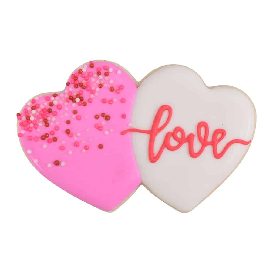 Decorated double heart-shaped sugar cookie with one pink and one white heart, featuring sprinkles and "love" written in red icing.