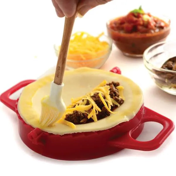 : Close-up of filling being added to dough inside the press, with a pastry brush applying egg wash.